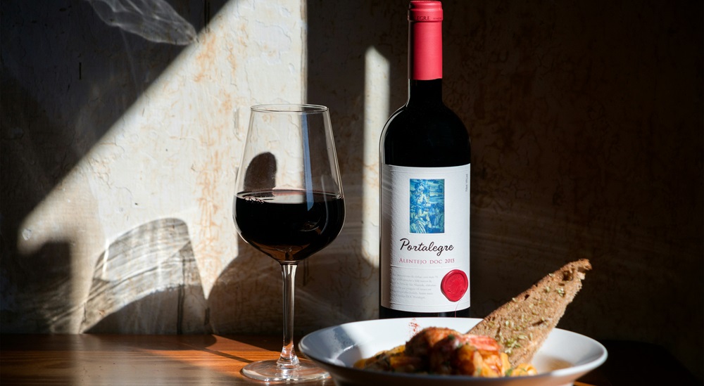 Rotweinglas neben einer Flasche Wein und einem Teller mit einer Speise